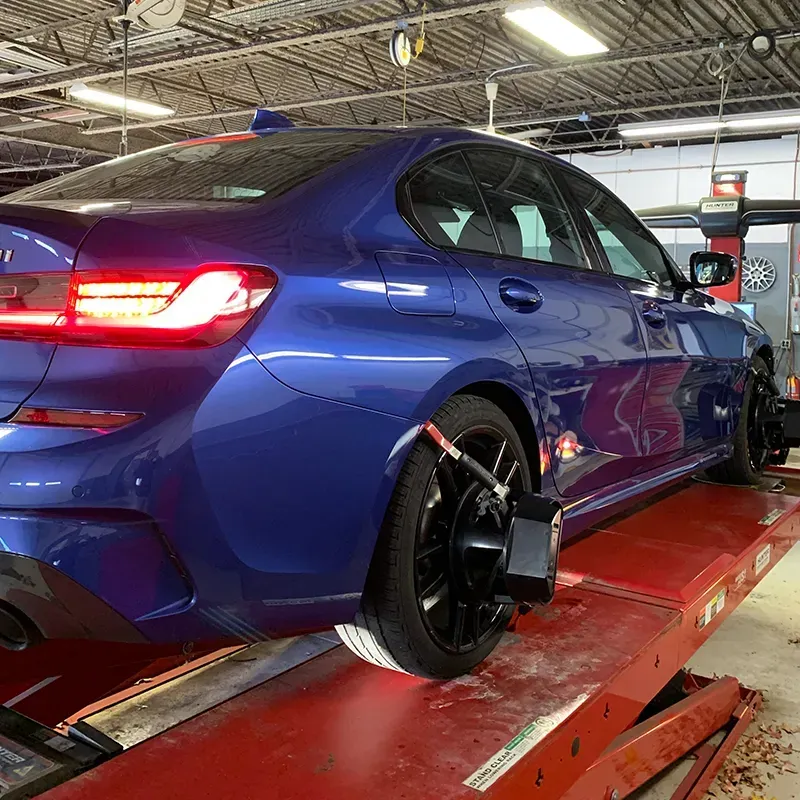 Blue sports sedan on a lift in an auto repair shop, viewed from the rear side.
