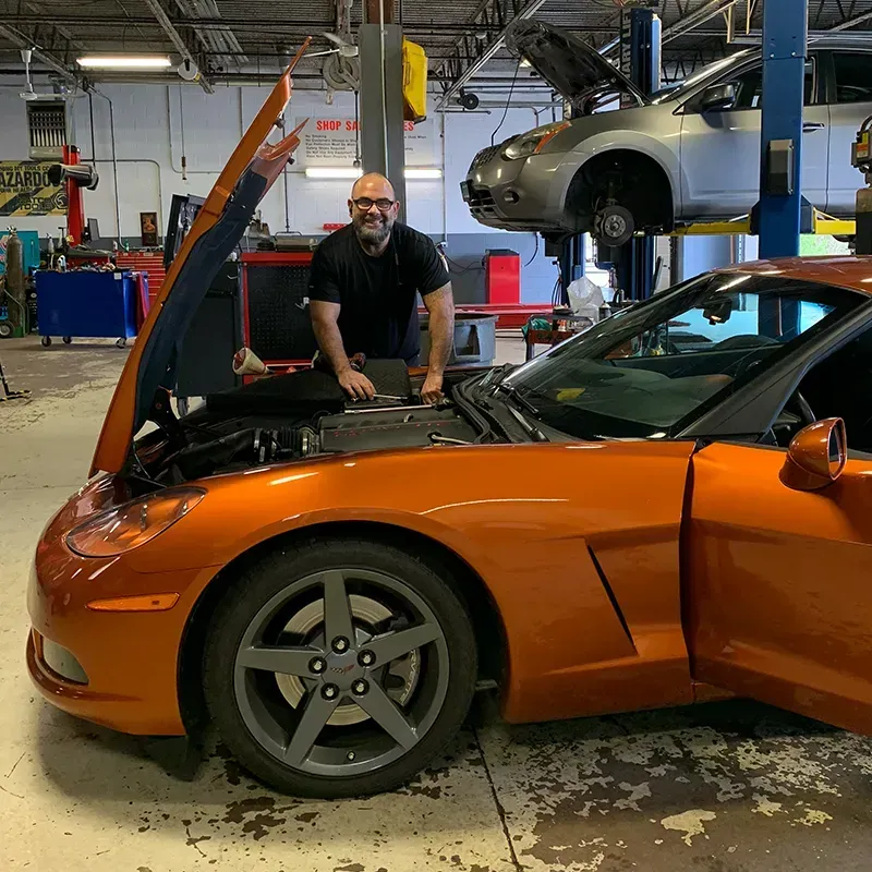 Mechanic working on orange sports car in auto repair shop with hood and door open