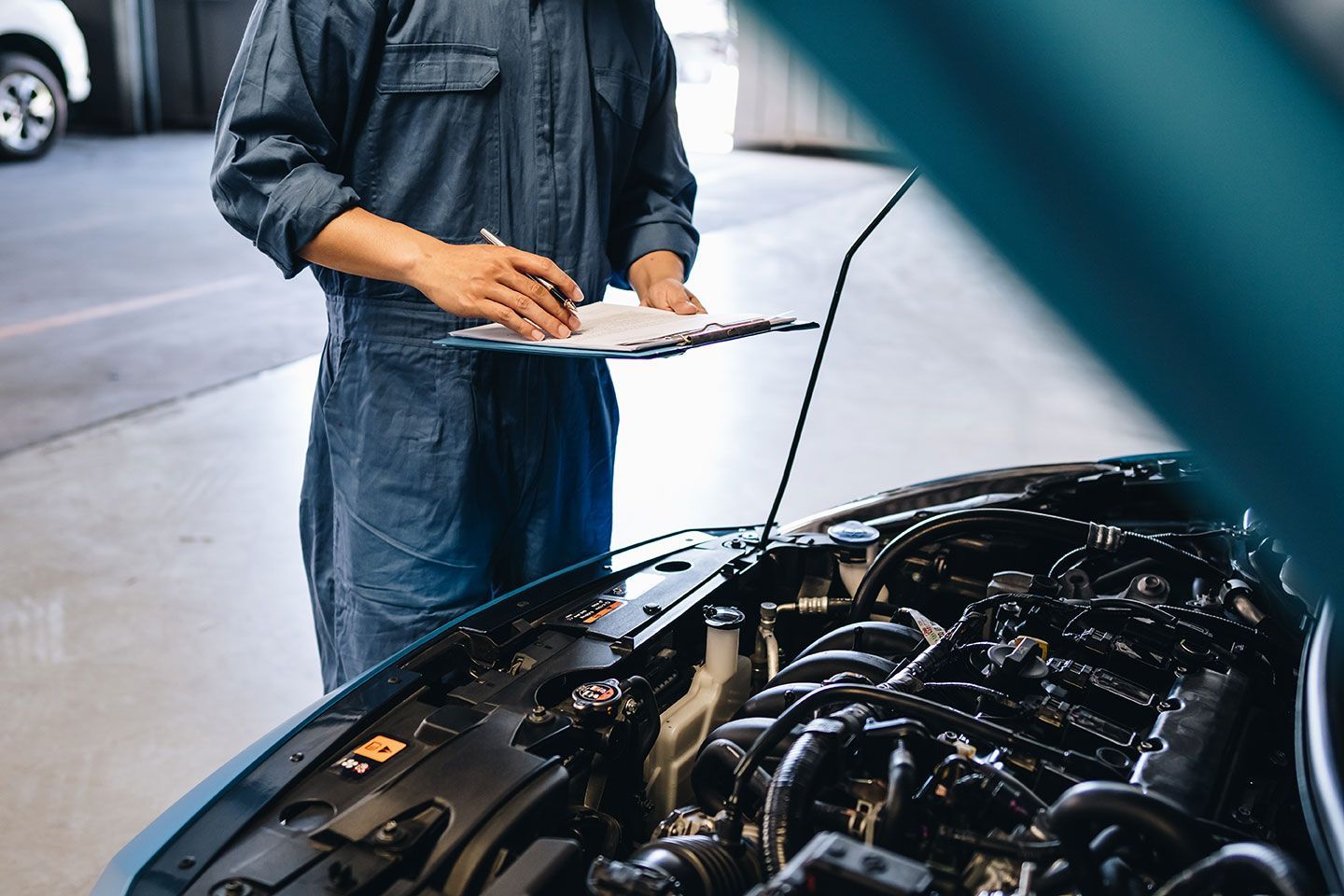 Mechanic holding clipboard beside a car engine with the hood open in a garage
