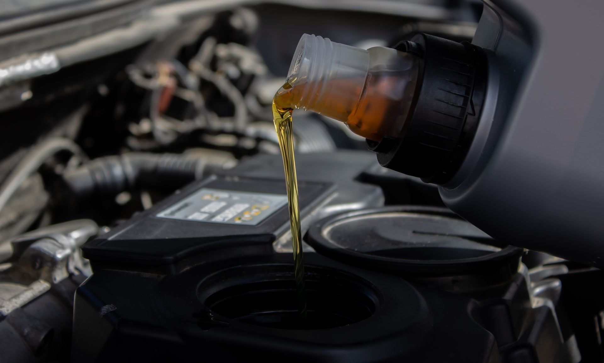 Oil being poured from a bottle into a car engine, with the hood open.