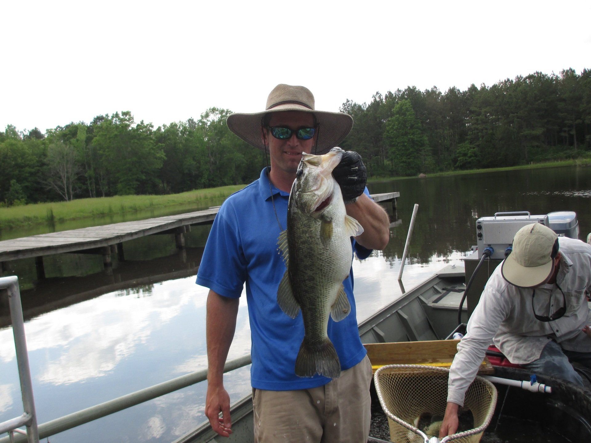 Man in blue shirt and hat holding a large fish on a boat, near a dock.