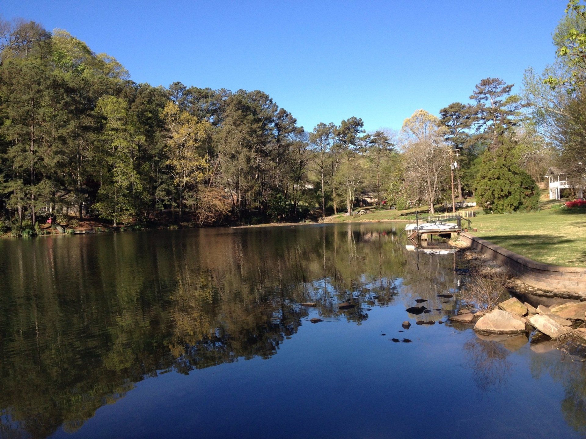 Calm lake reflecting trees and a clear blue sky. A small dock is visible on the right side.