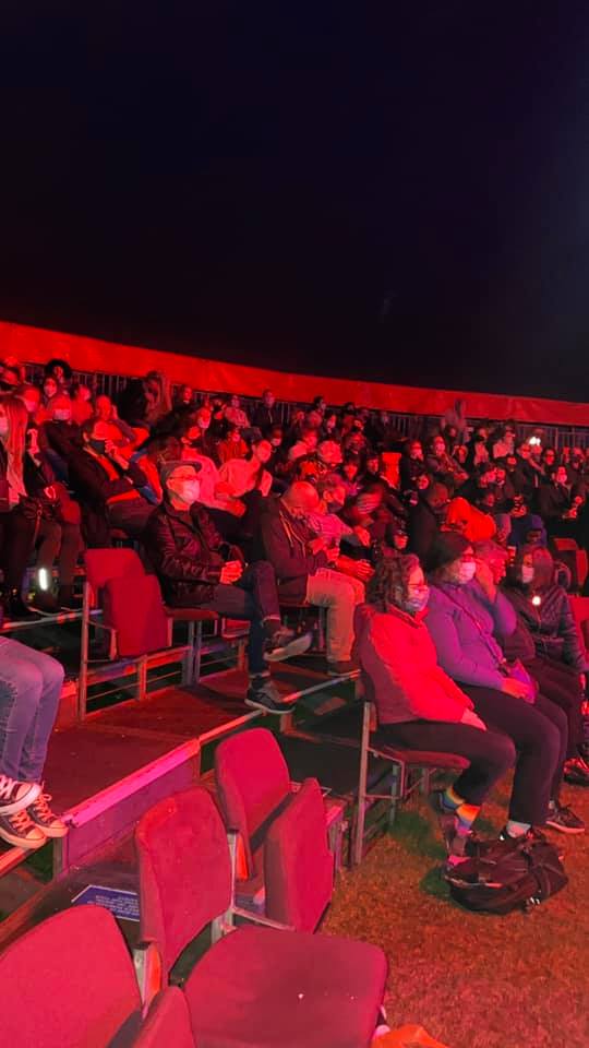 A crowd of people are sitting in red chairs at a concert.