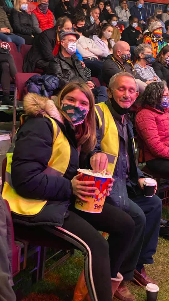 A group of people wearing face masks are sitting in a stadium eating popcorn.