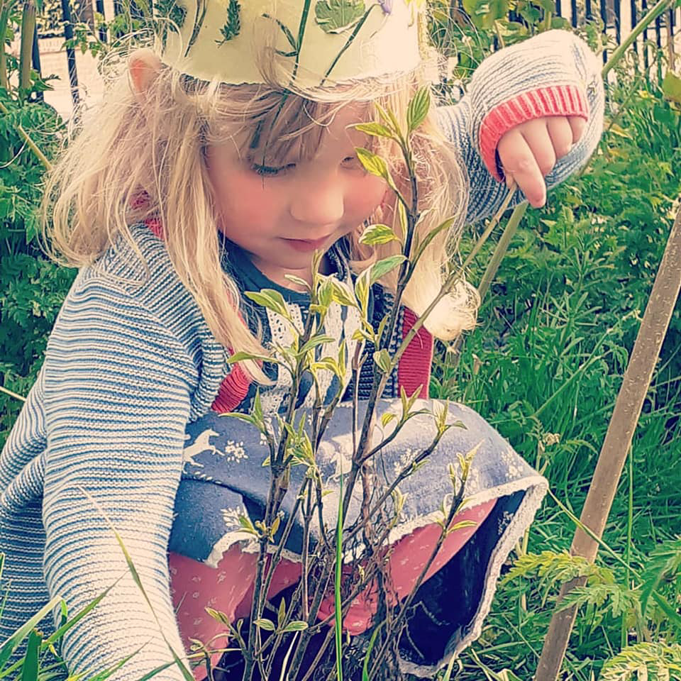 A little girl wearing a crown is kneeling down in the grass