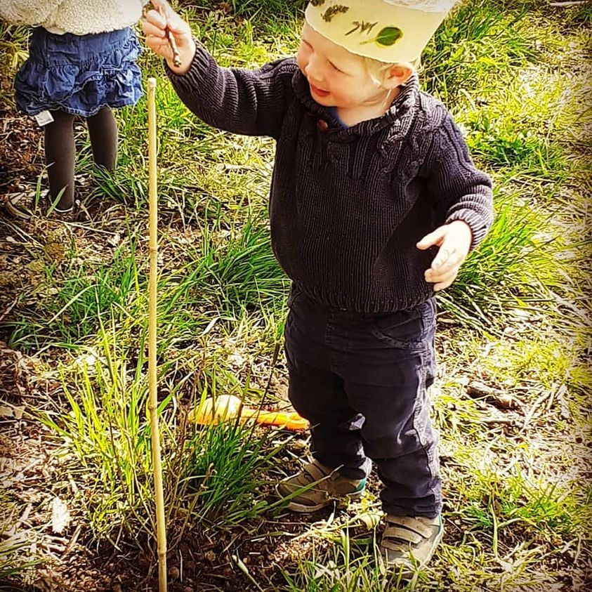 A little boy wearing a crown is measuring a stick in the grass