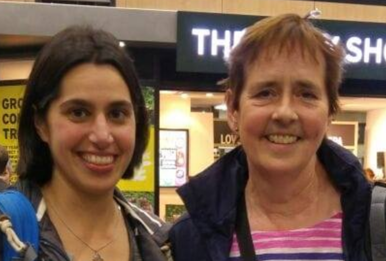 Two women are posing for a picture in front of a grocery store