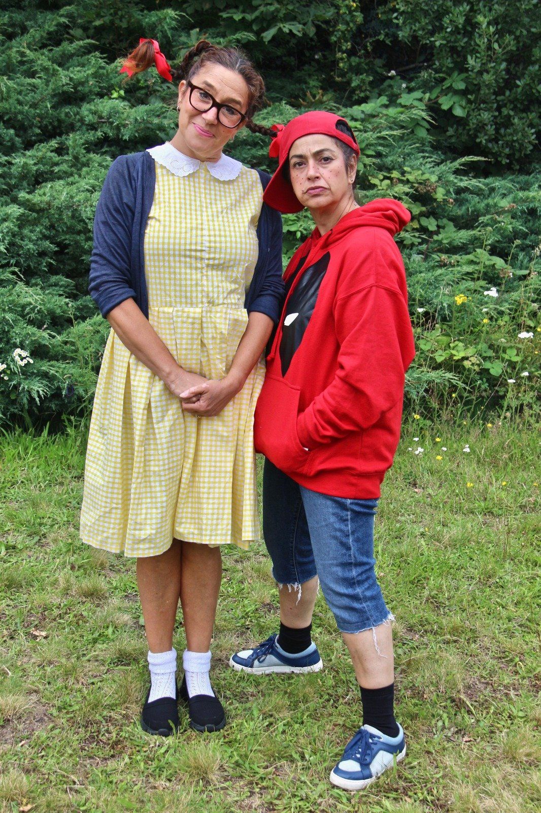 A woman in a yellow dress and a man in a red hoodie are standing next to each other in the grass.