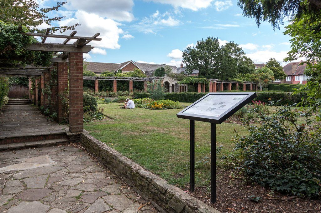 A stone walkway leading to a garden with a sign in the foreground.