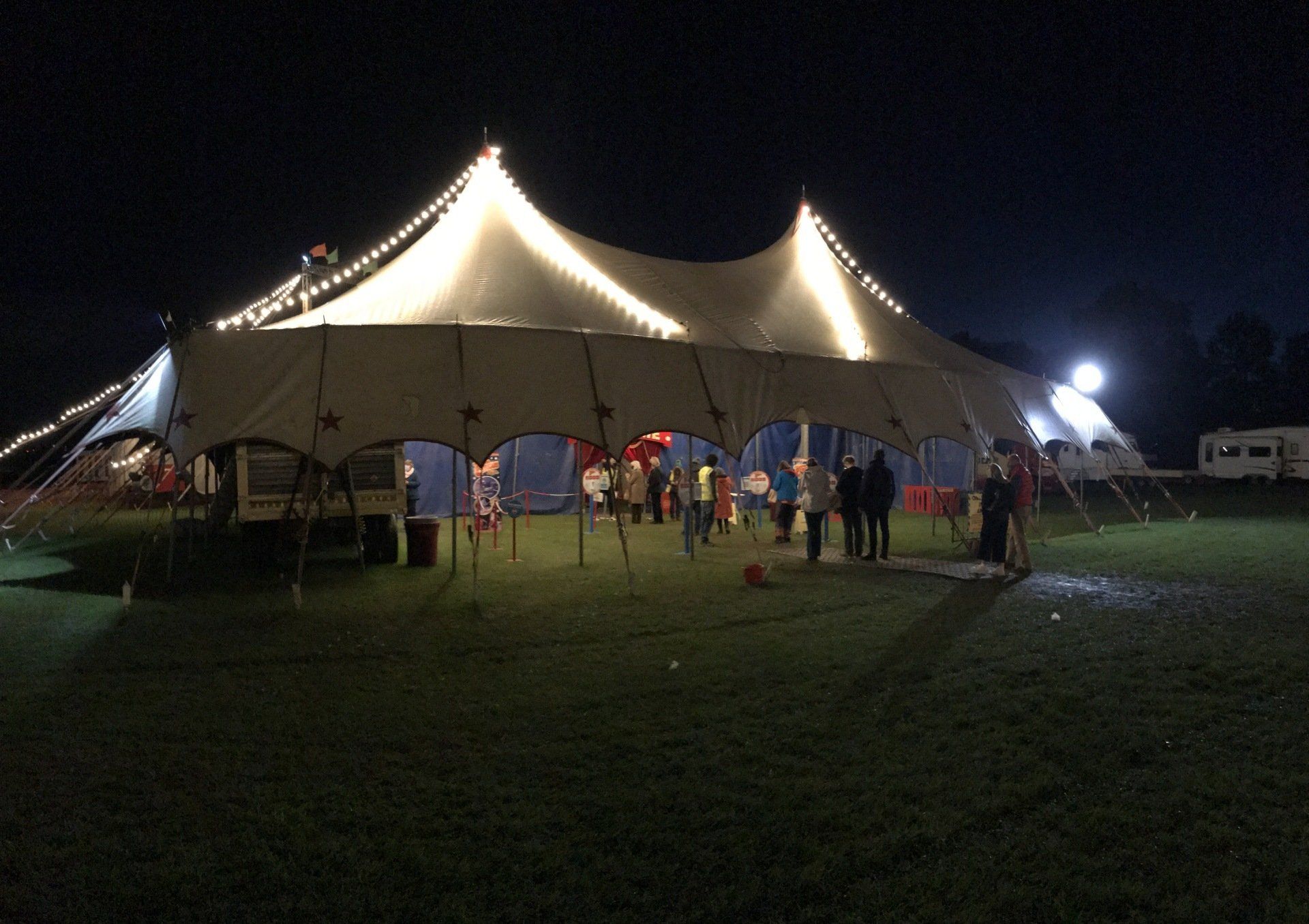 A large circus big top tent is lit up at night in a field.