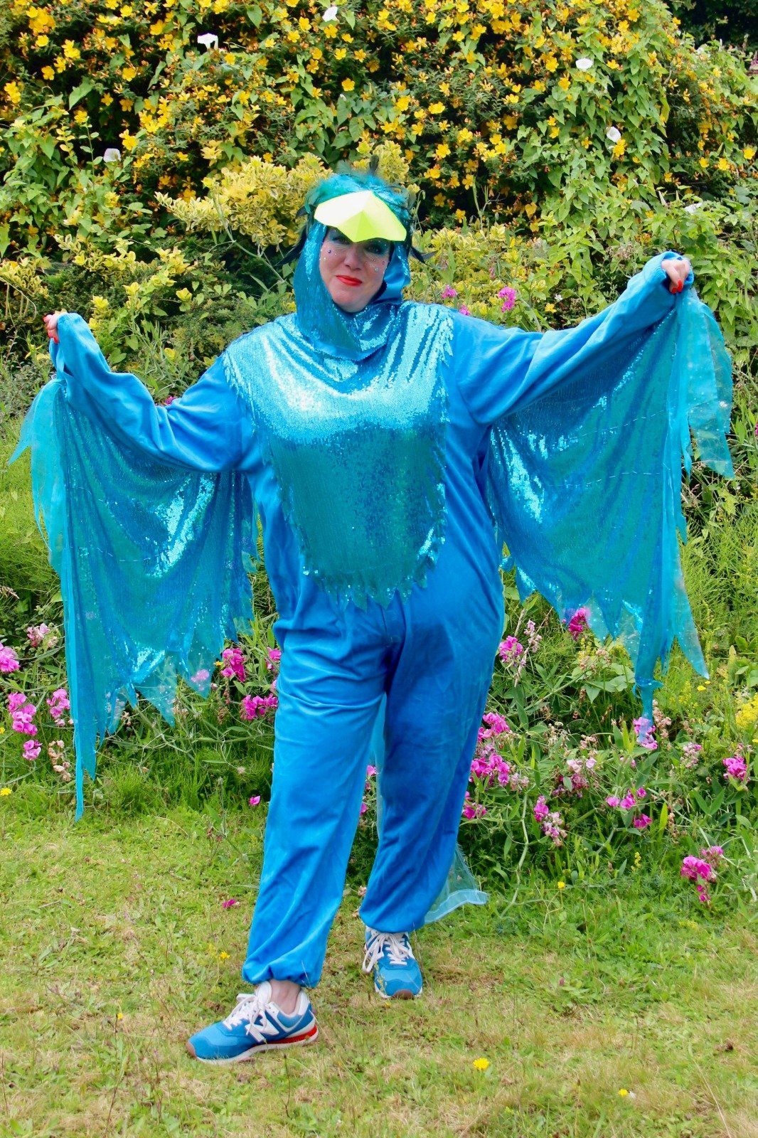 A woman in a blue bird costume is standing in the grass.