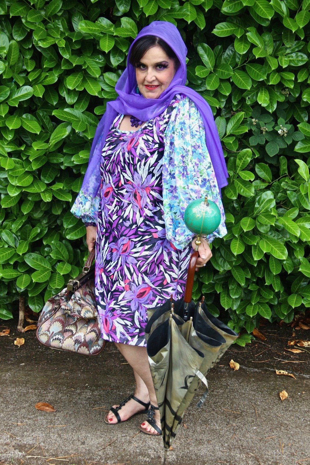 A woman in a purple dress is holding an umbrella and a purse.