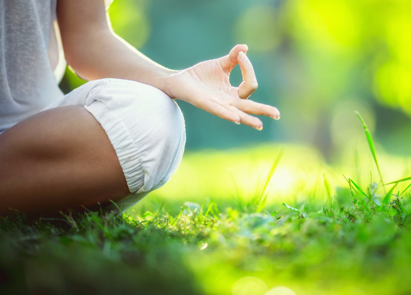 A woman is sitting on the grass in a lotus position.