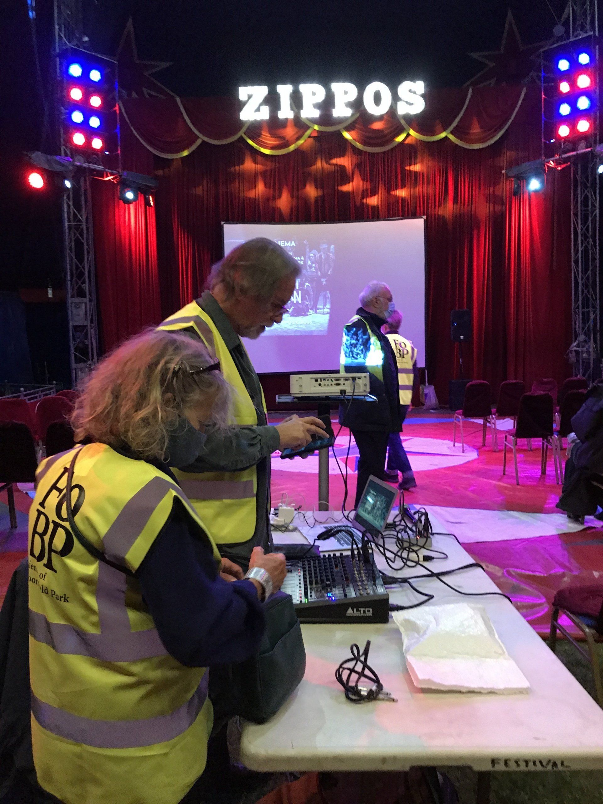 A group of people are working on a stage in front of a sign that says zippos.