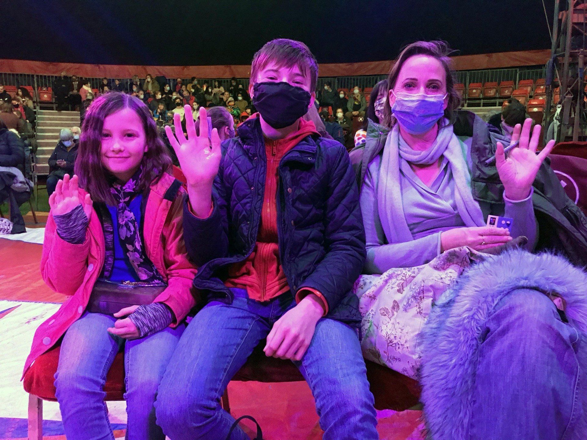A group of people wearing face masks are sitting on a bench in a circus.