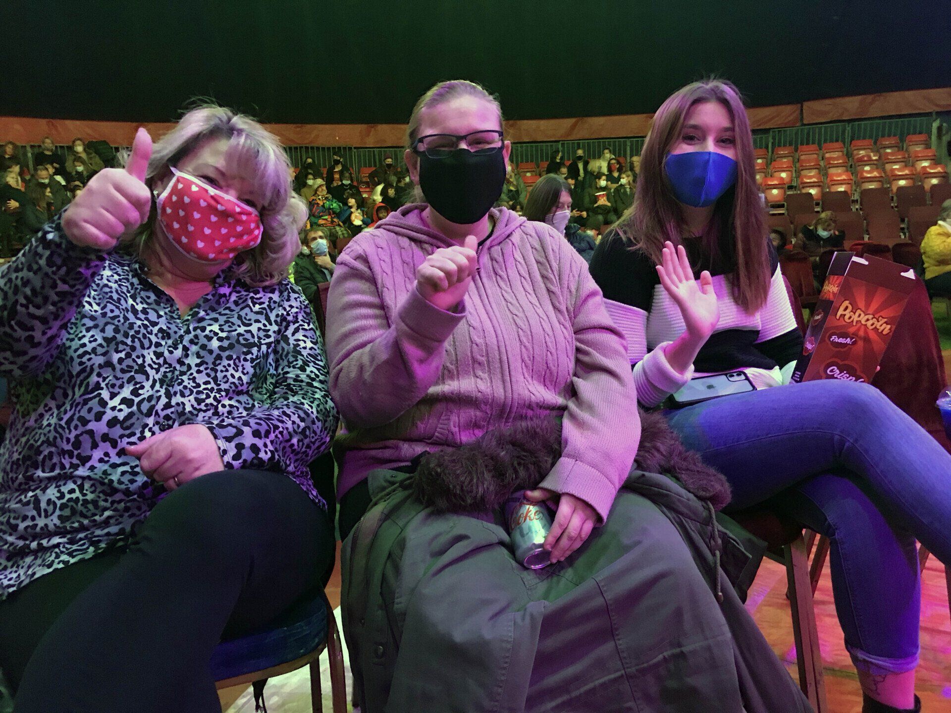 Three women wearing face masks are sitting in chairs at a concert.