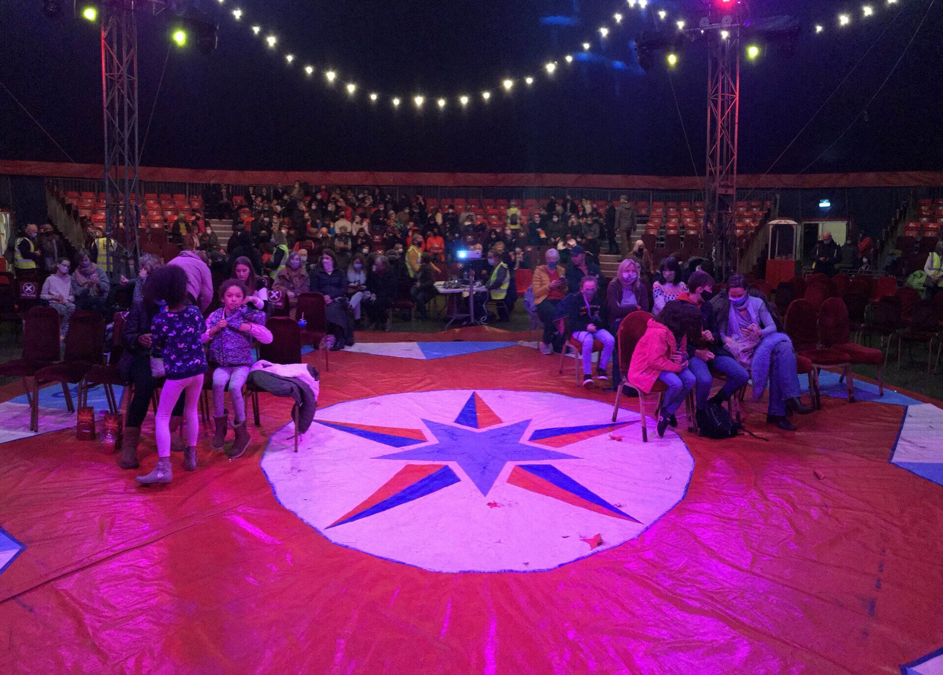 A group of people are sitting on the floor of a circus tent.