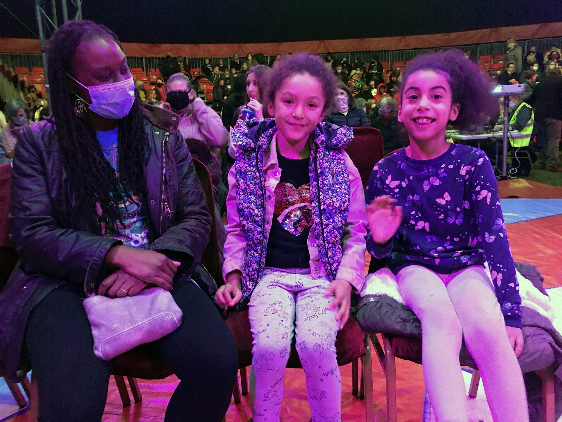 A woman wearing a mask is sitting next to two little girls.