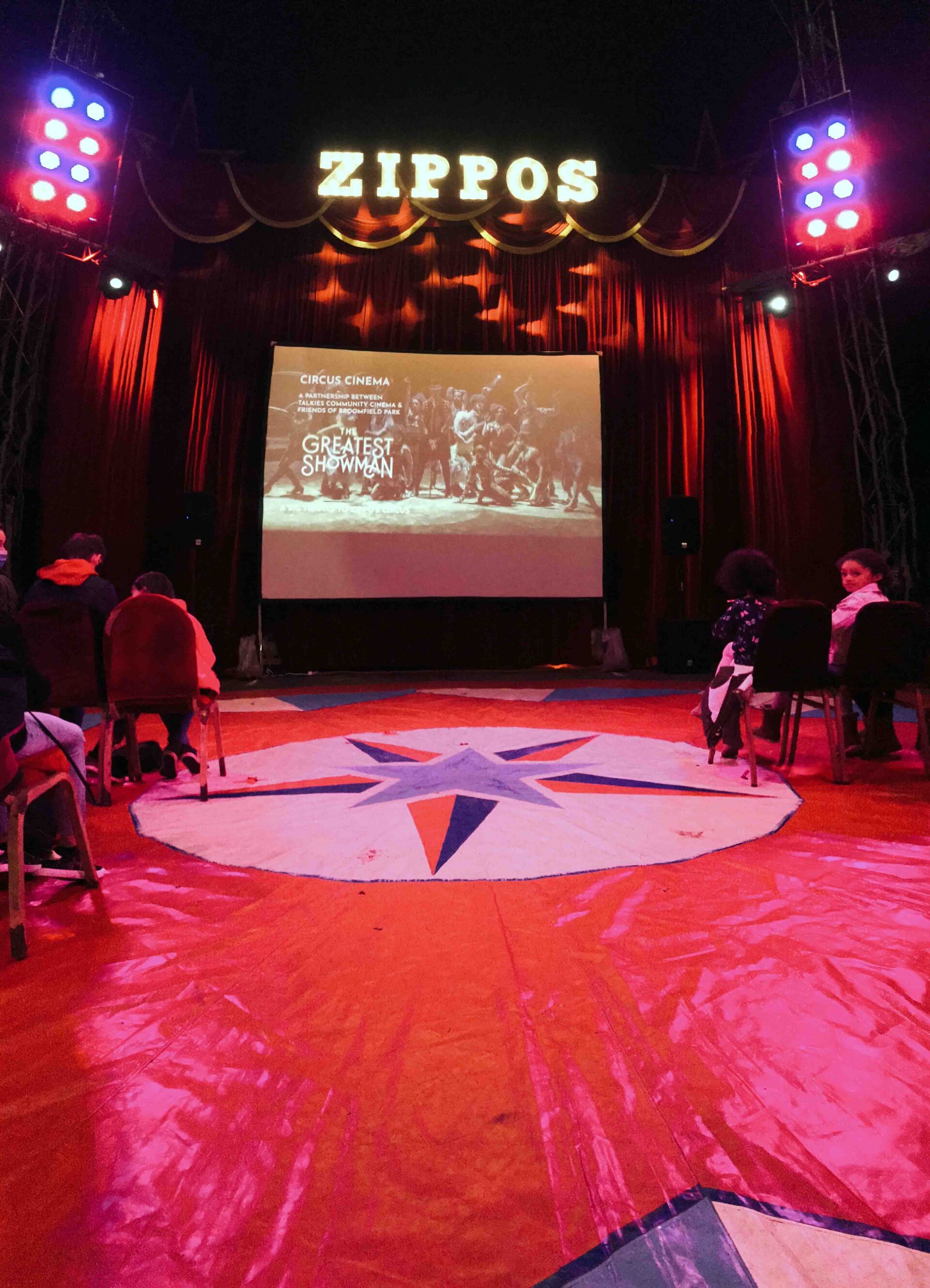 A group of people are sitting in front of a screen that says zippos