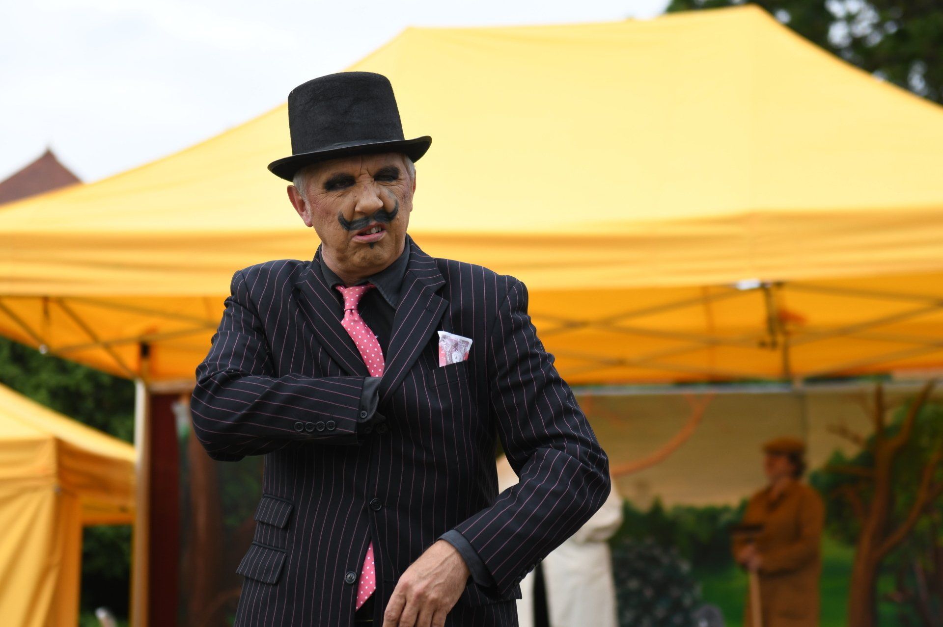 A man in a suit and top hat is standing in front of a yellow tent.