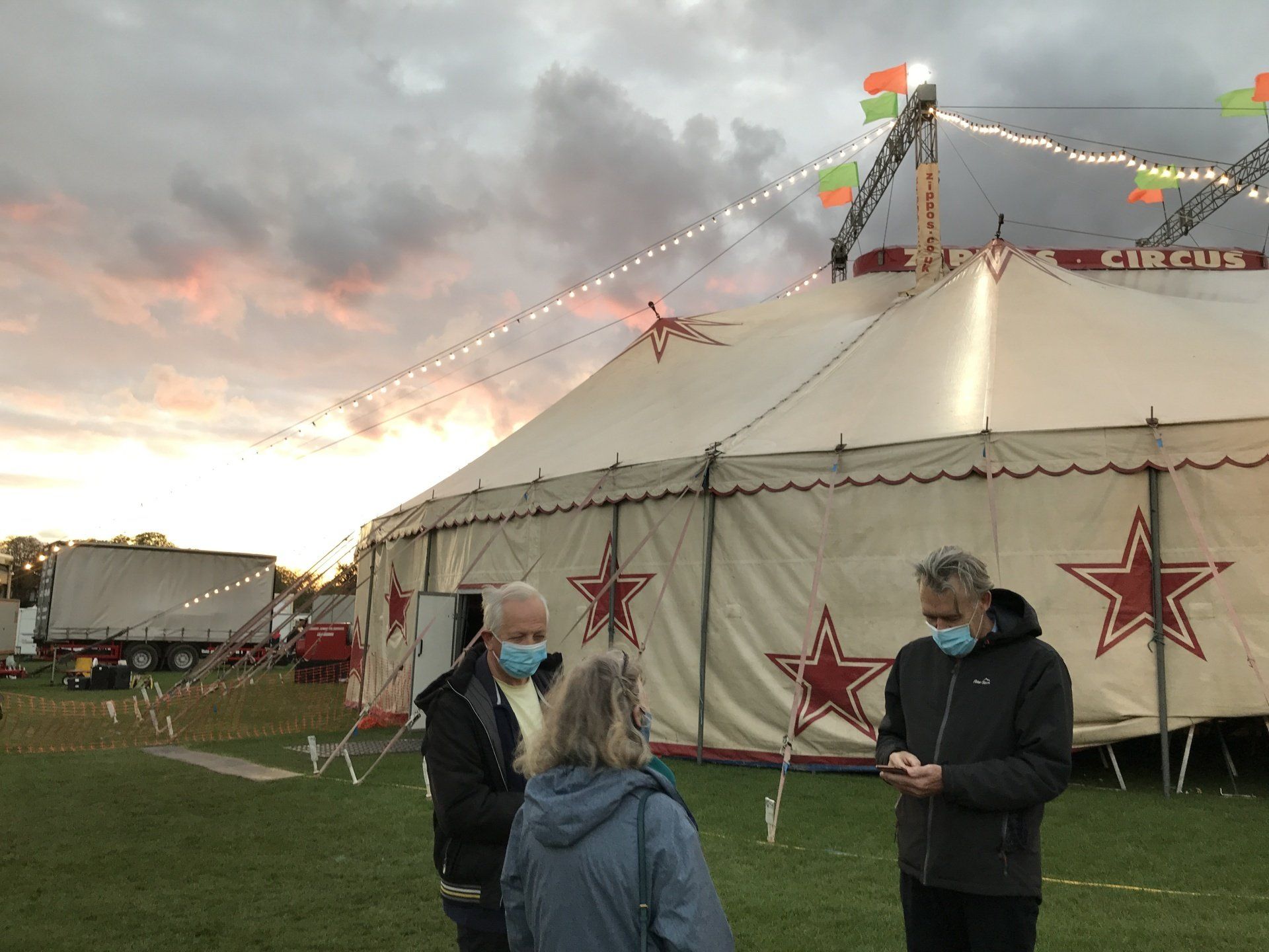 A group of people wearing face masks are standing in front of a circus tent.