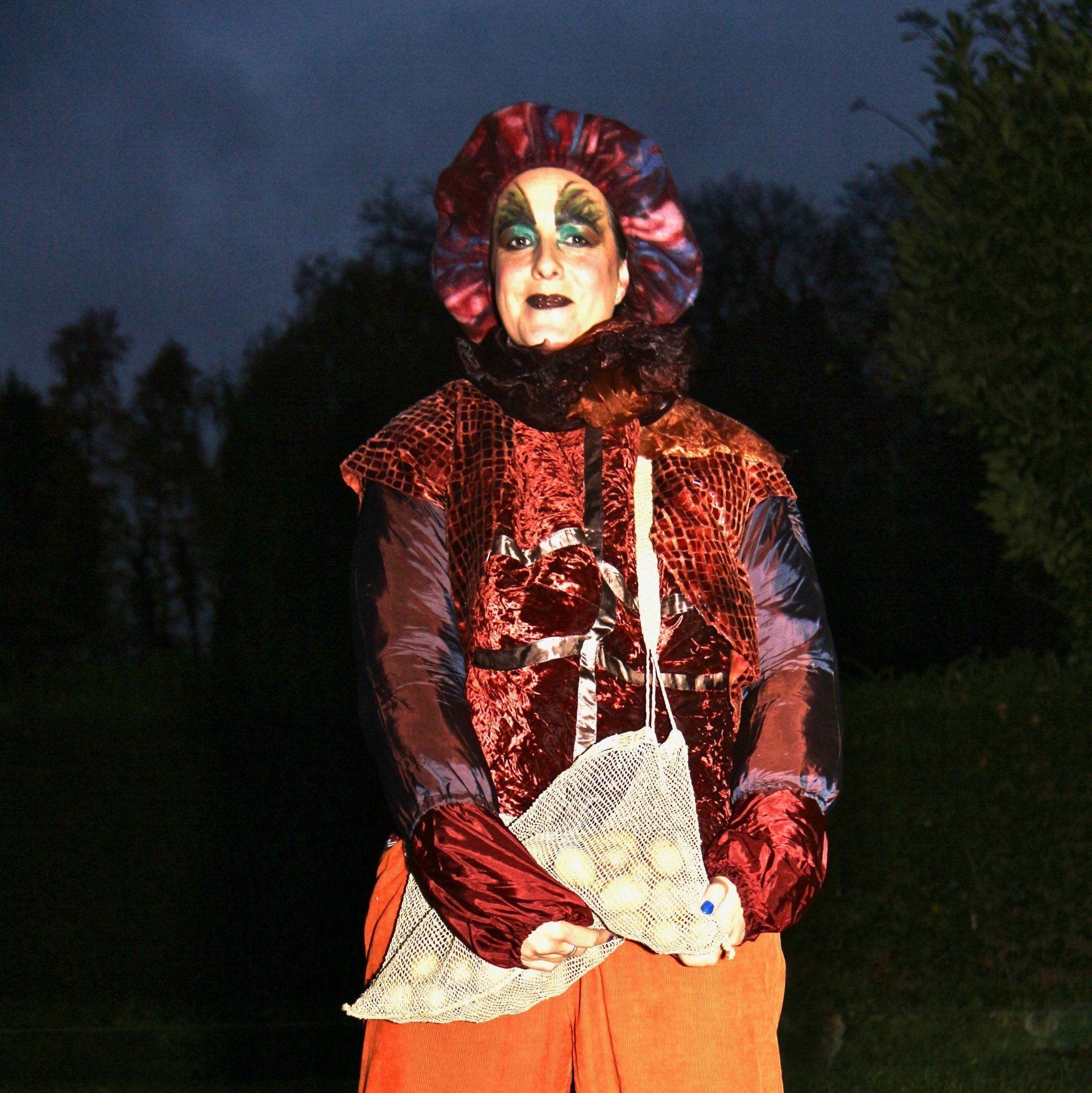 A woman in a clown costume is holding a bag of potatoes