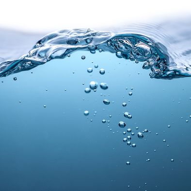 A close up of a wave in the ocean with bubbles coming out of it.