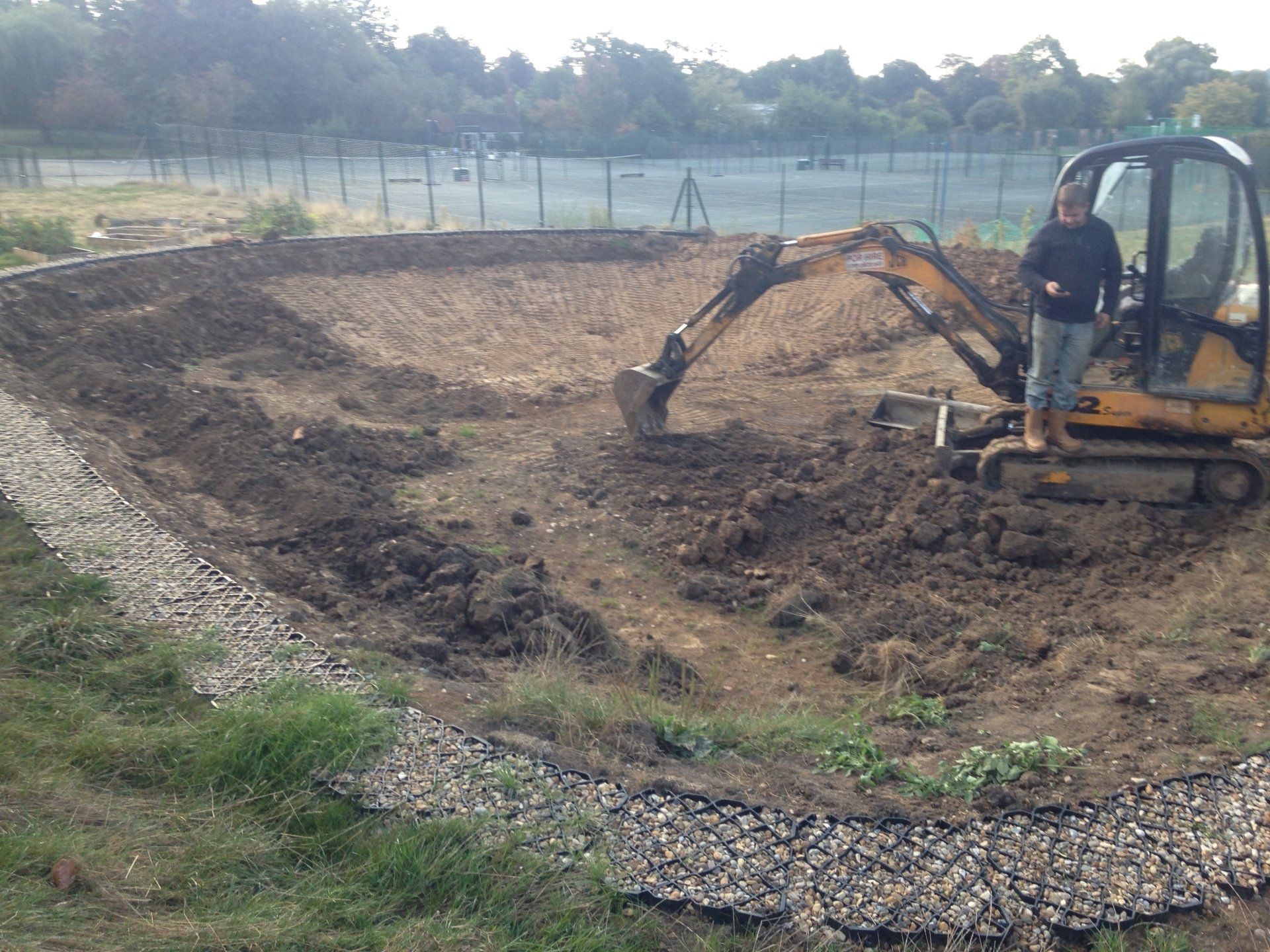 A man is standing next to an excavator in a dirt field.