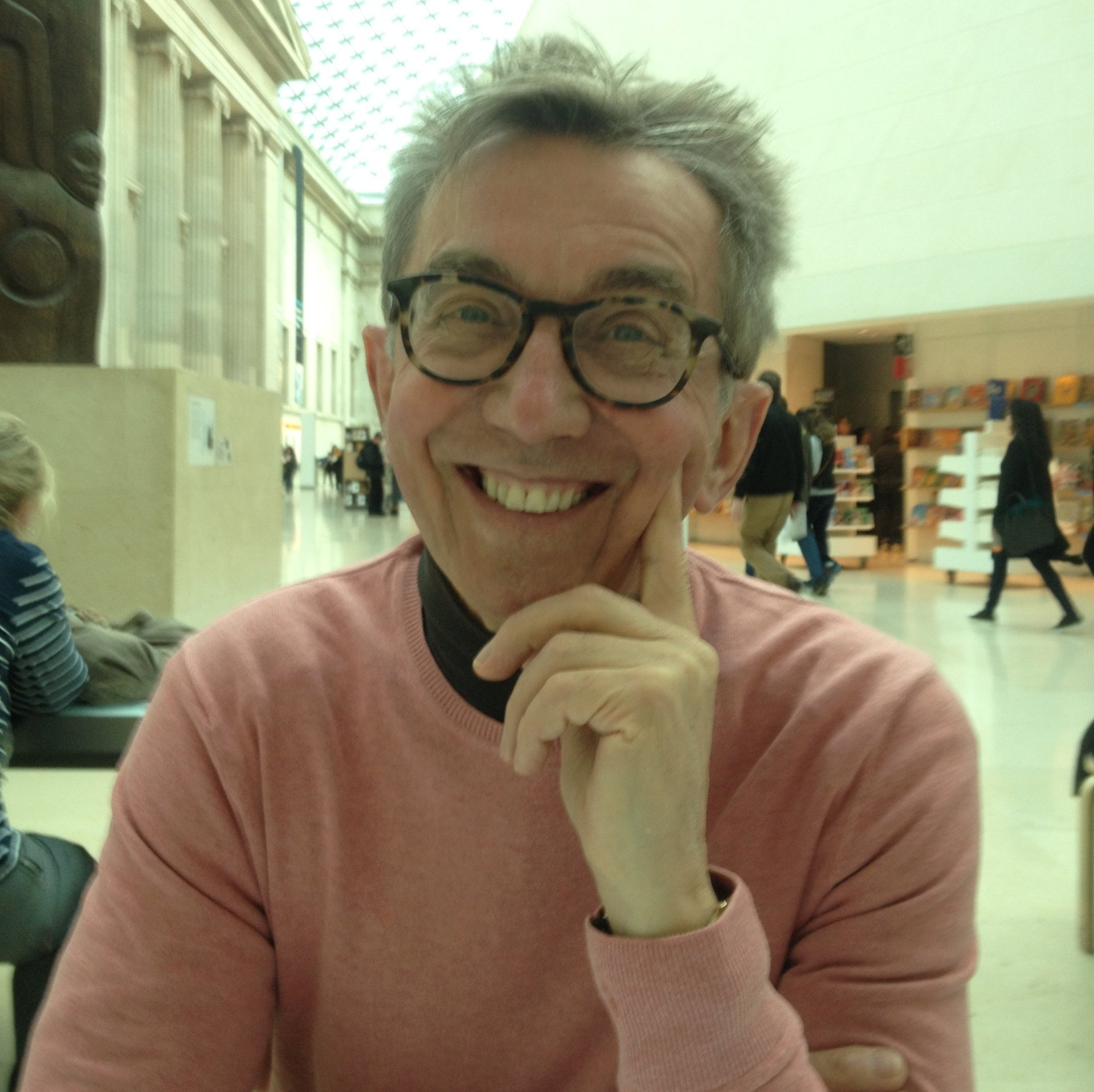 A man wearing glasses and a pink sweater smiles for the camera