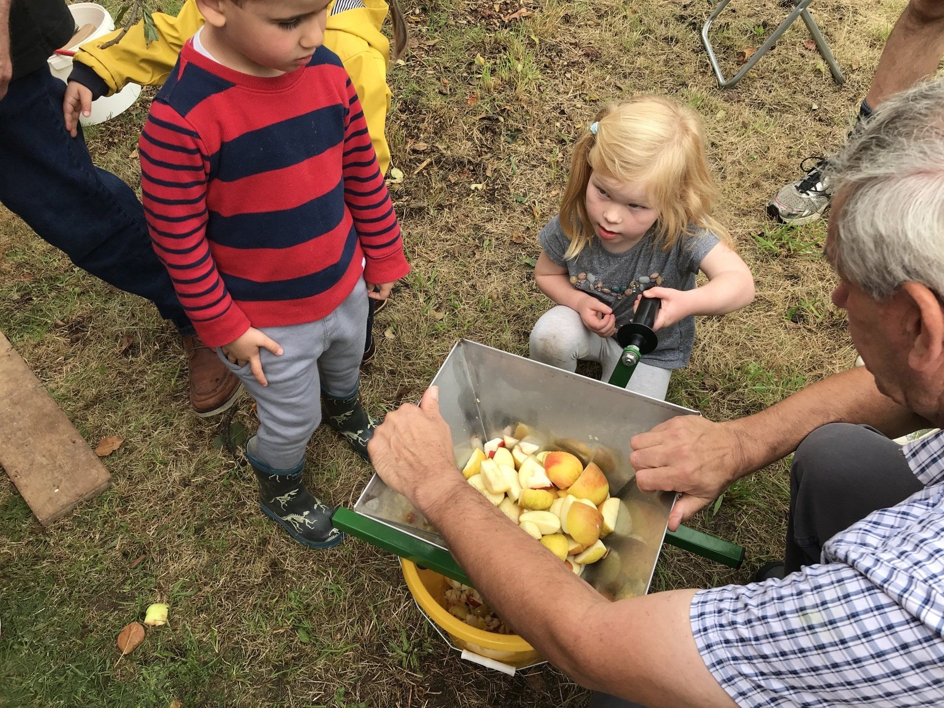 A man is holding a bucket of apples in front of a group of children.