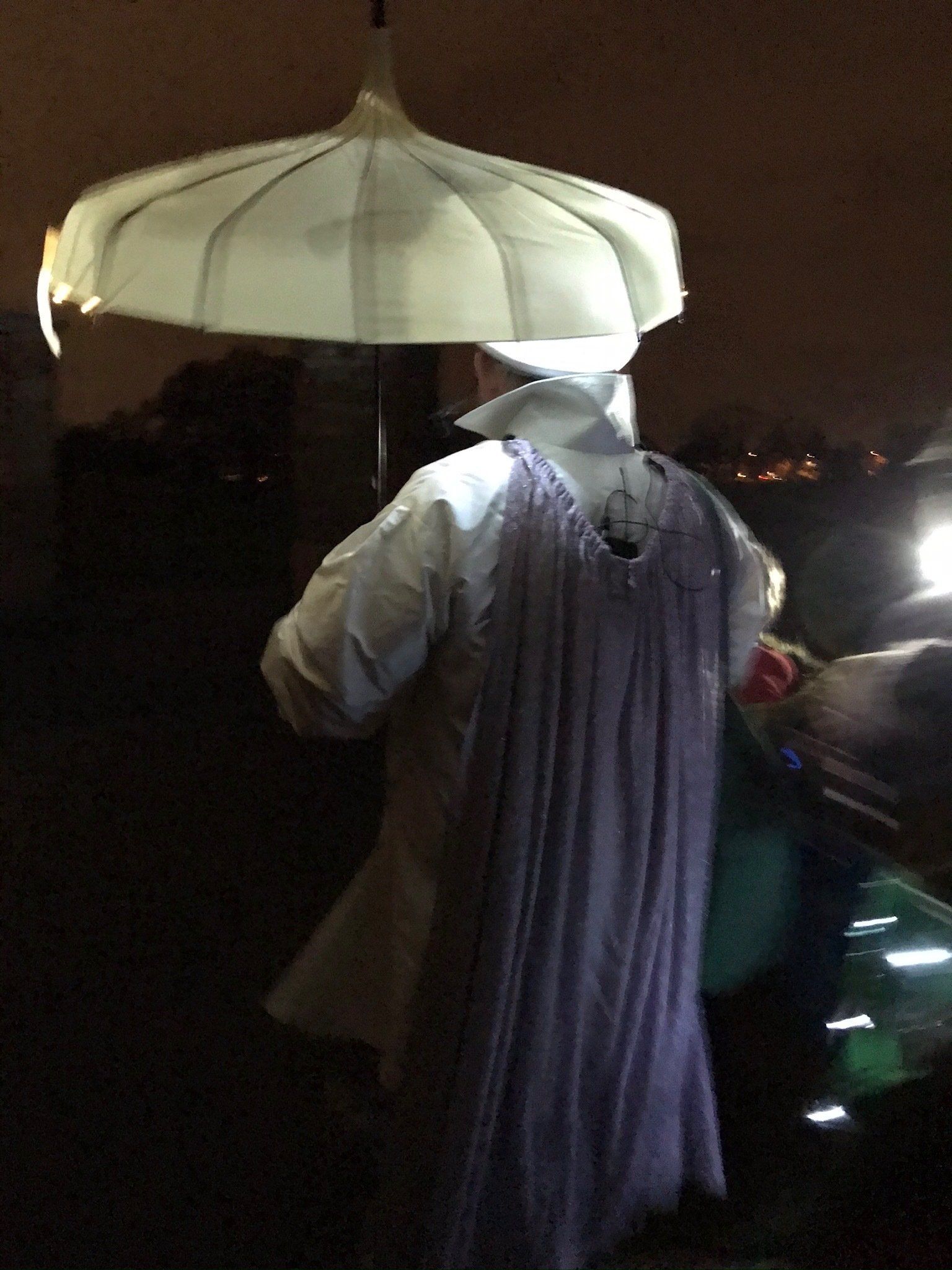 A person in a purple dress is holding an umbrella in the dark.