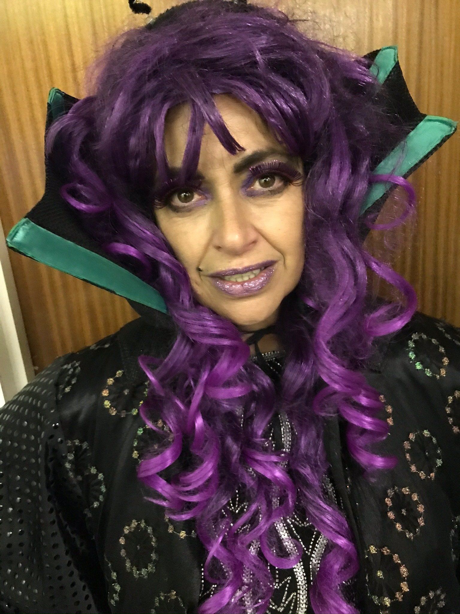 A woman is wearing a purple wig and a black cape.