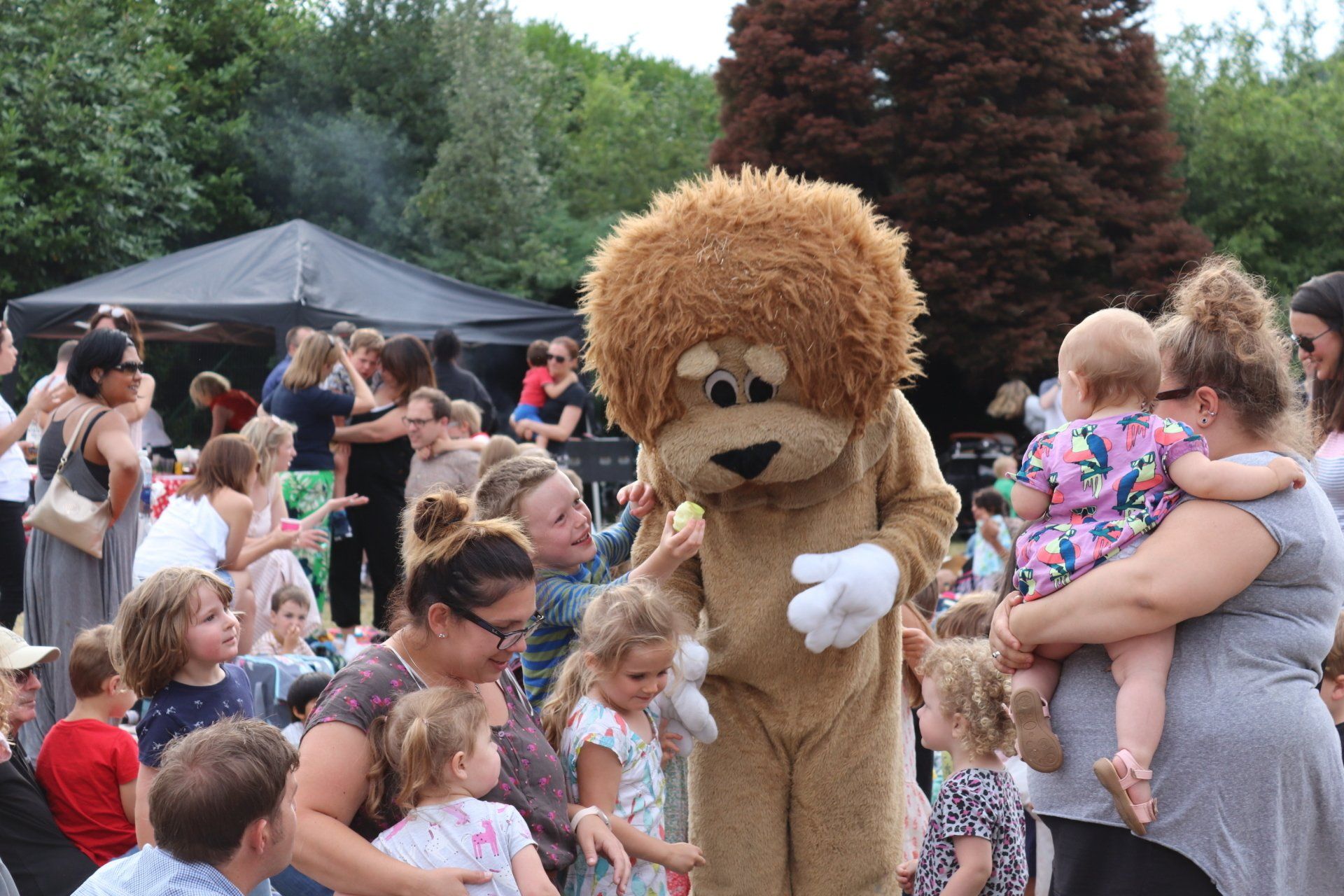 A lion mascot is standing in front of a crowd of people.