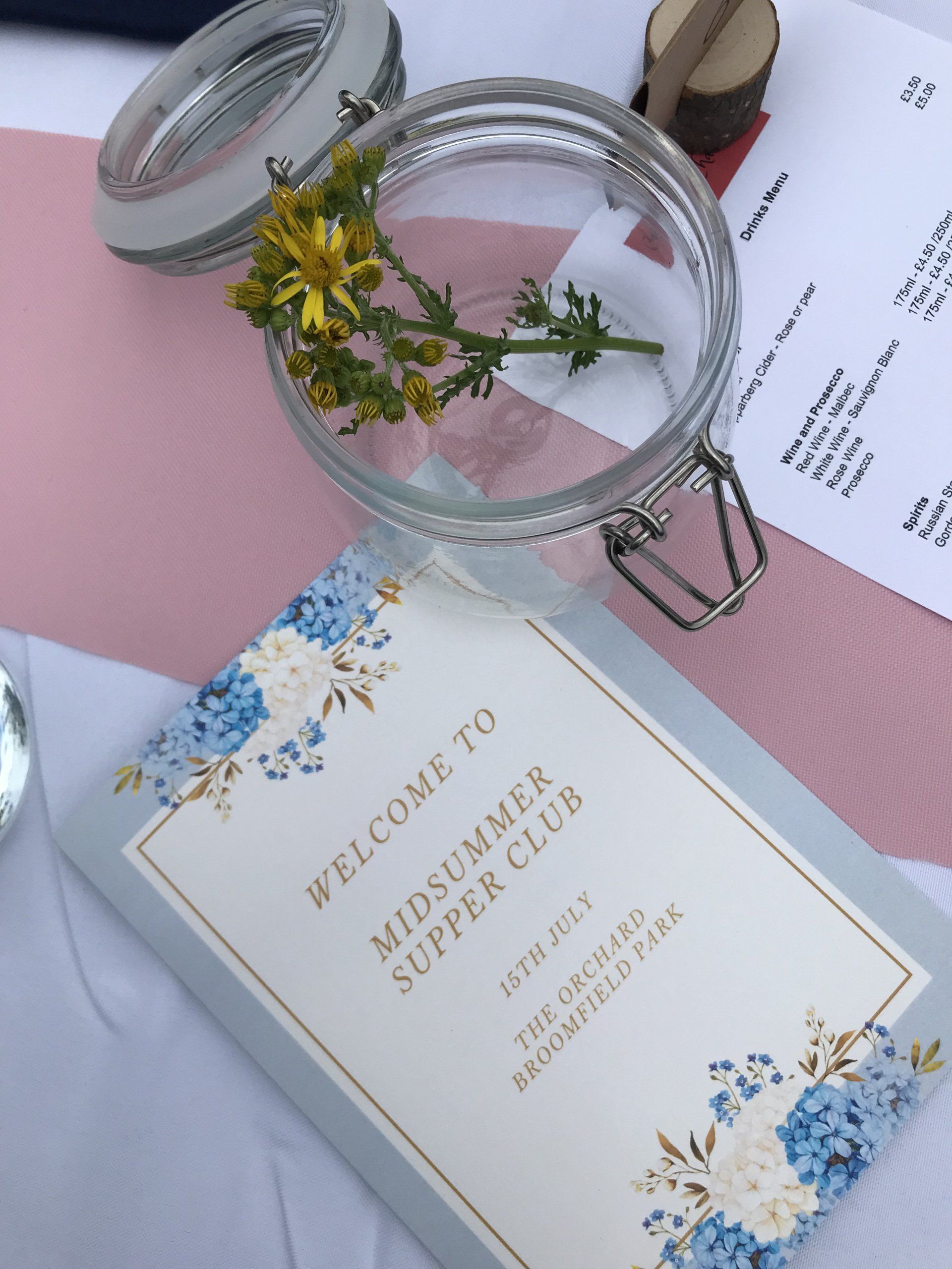 A welcome to midsummer supper club card is on a table