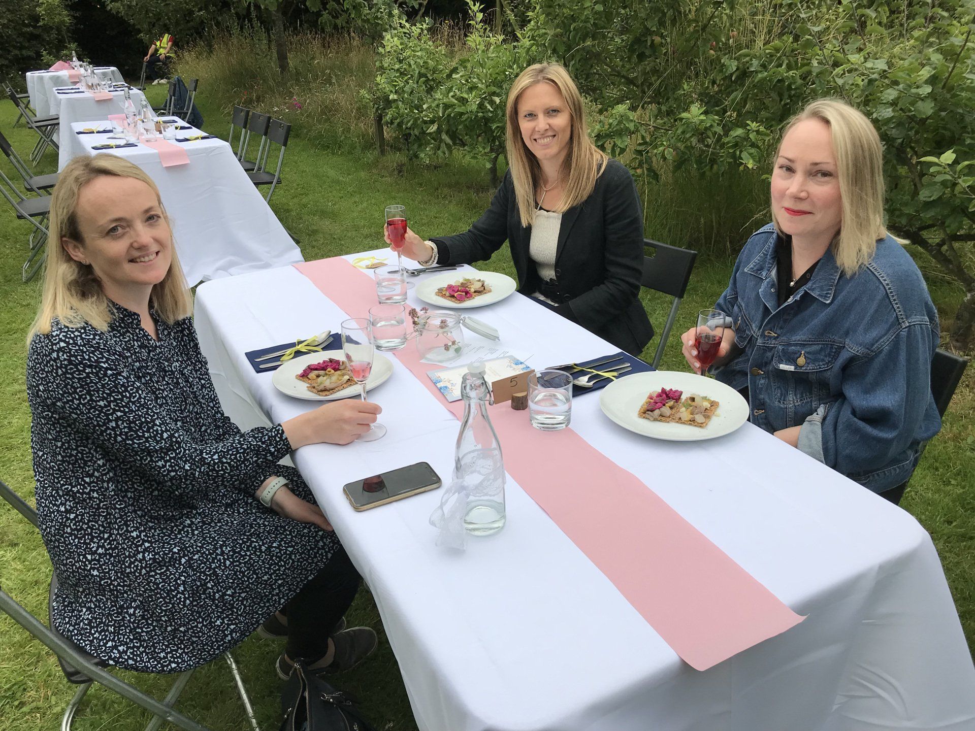 Three women are sitting at a long table with plates of food.