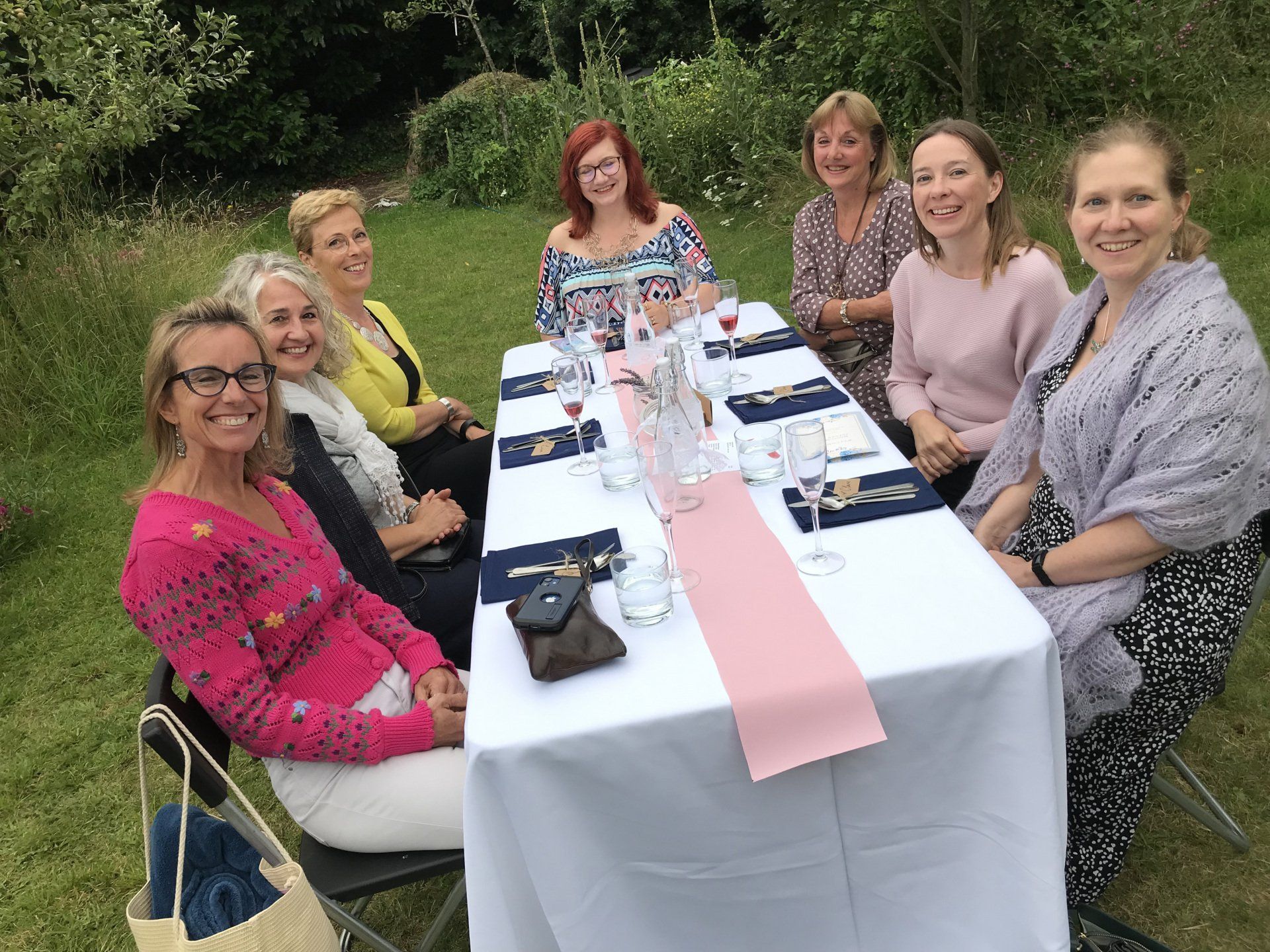 A group of women are sitting around a table in the grass.