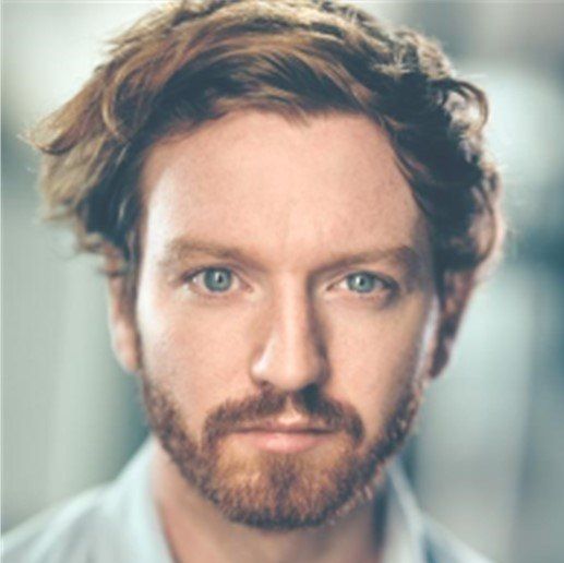 A man with a beard and long hair looks at the camera