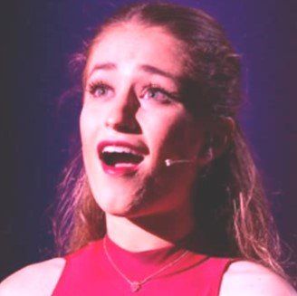 A woman in a red top is singing into a microphone.