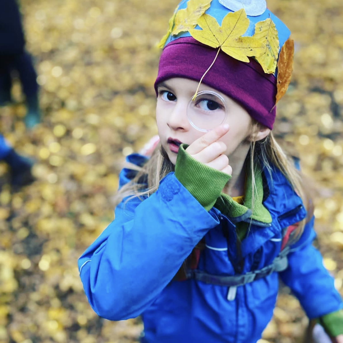 A little girl wearing a blue jacket and a purple hat with leaves on it