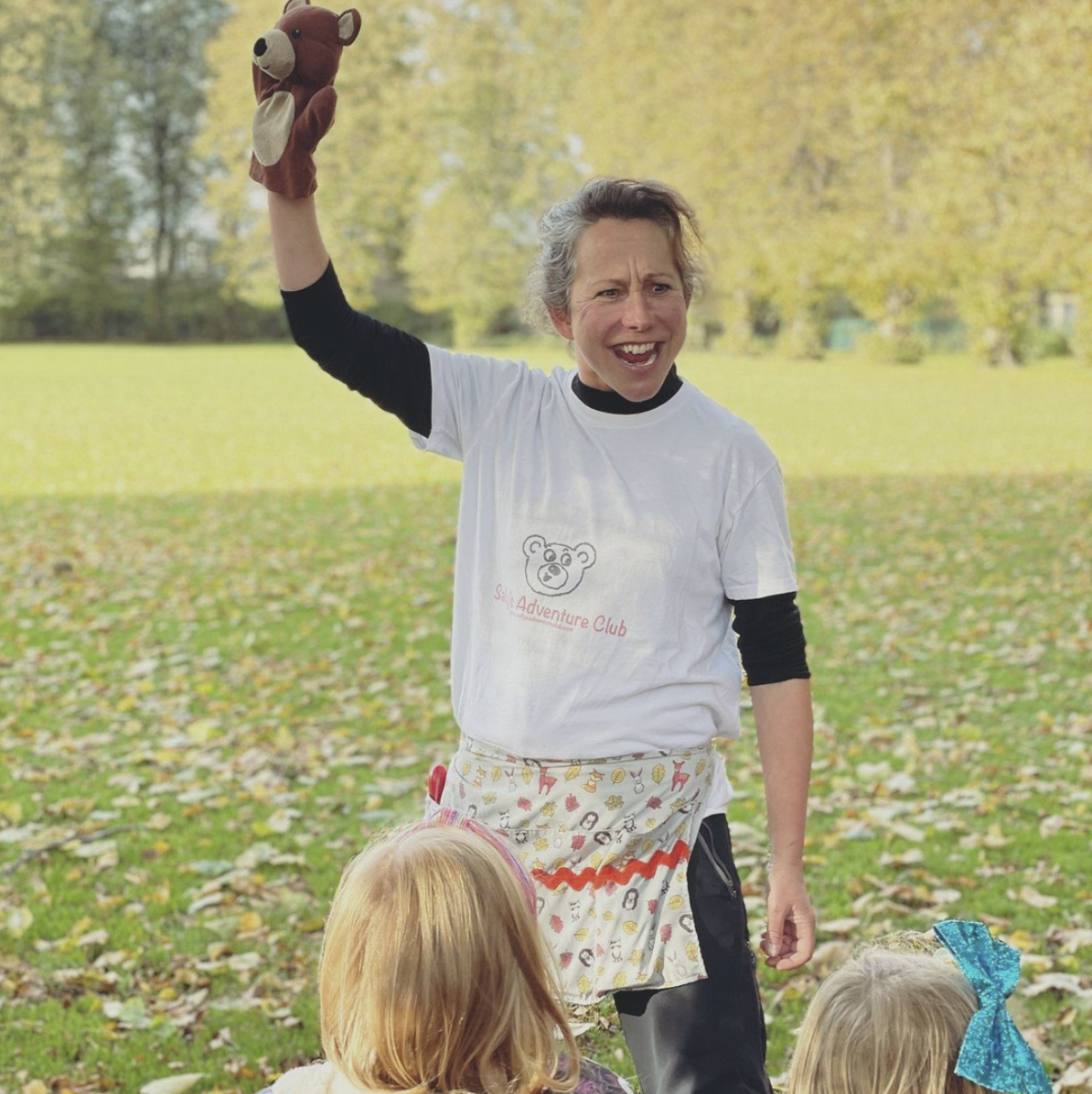 A woman is holding a teddy bear in her hand in a park