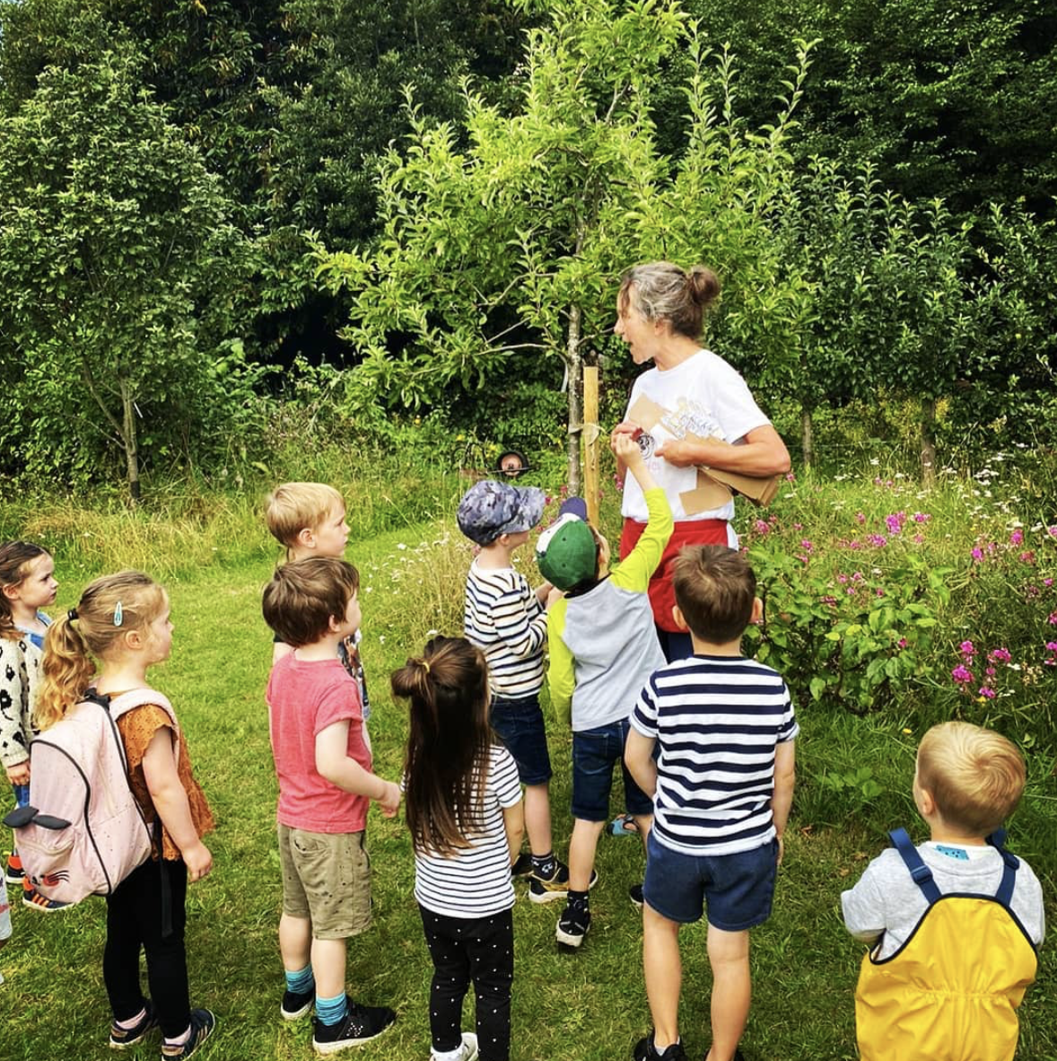 A woman is talking to a group of children in a field.