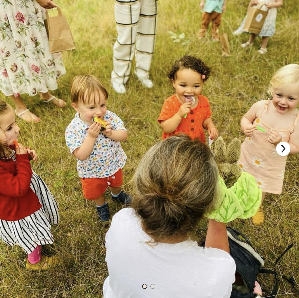 A group of children are standing around a woman in the grass.