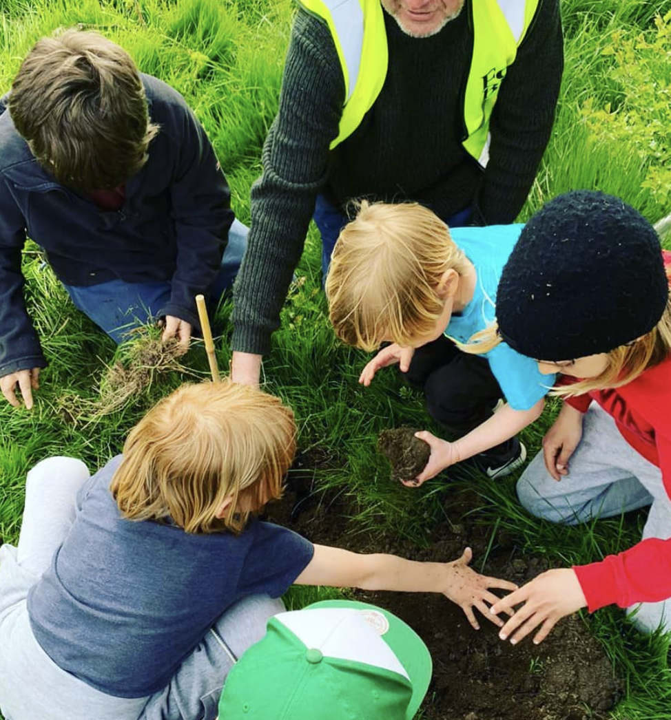 A group of children are kneeling in the grass playing with dirt