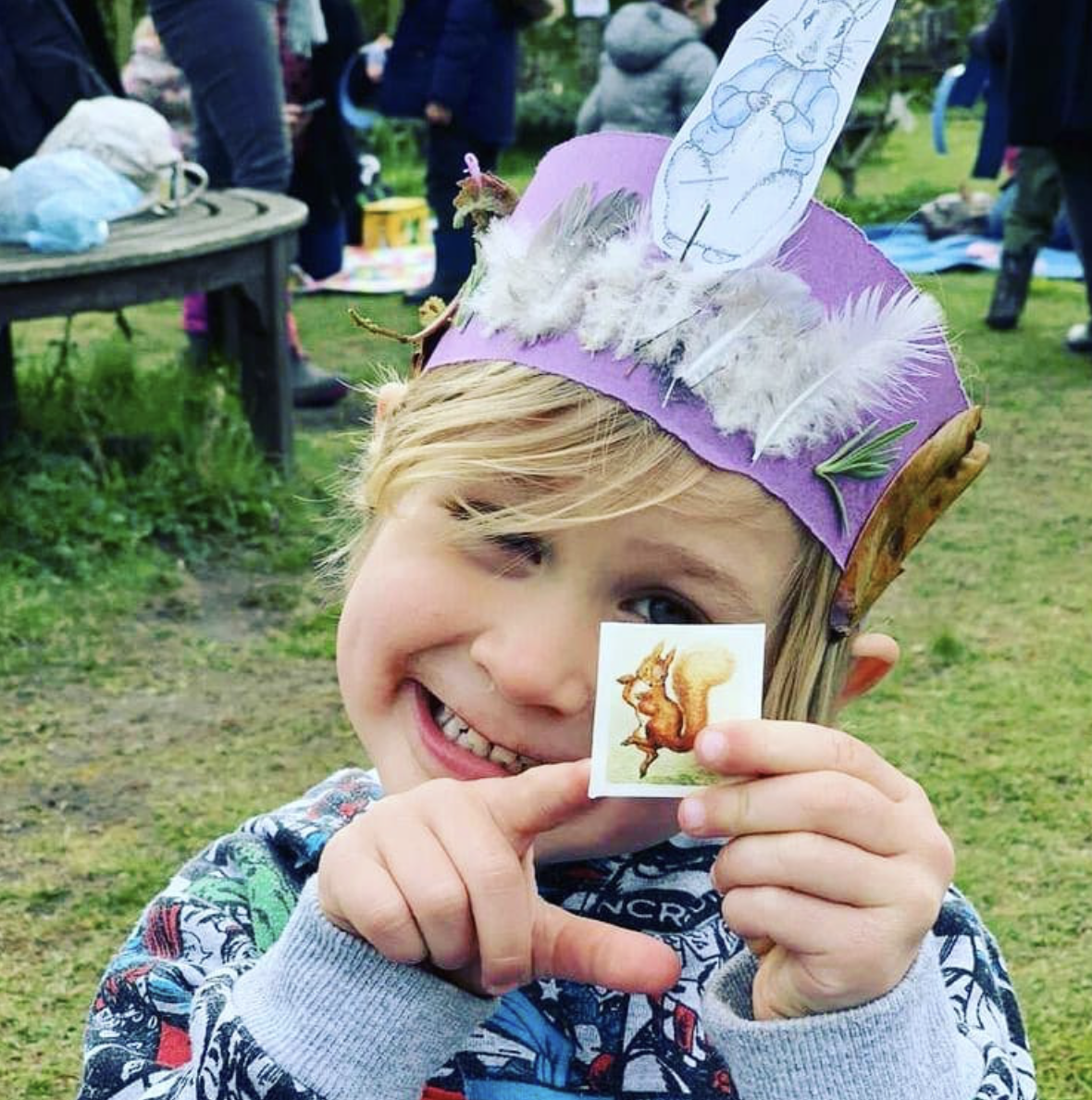 A young boy wearing a purple hat is holding a picture of a squirrel