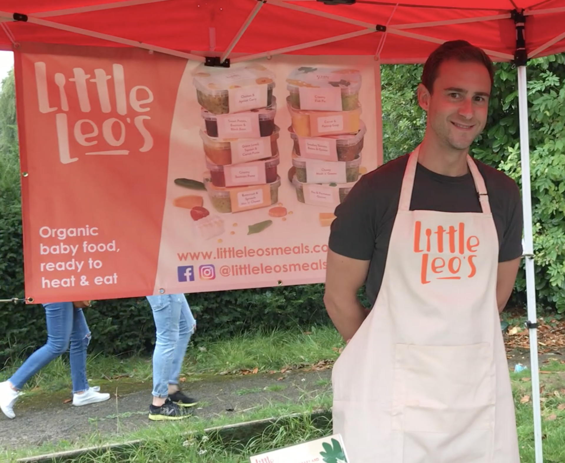 A man in an apron is standing in front of a sign that says little leo 's