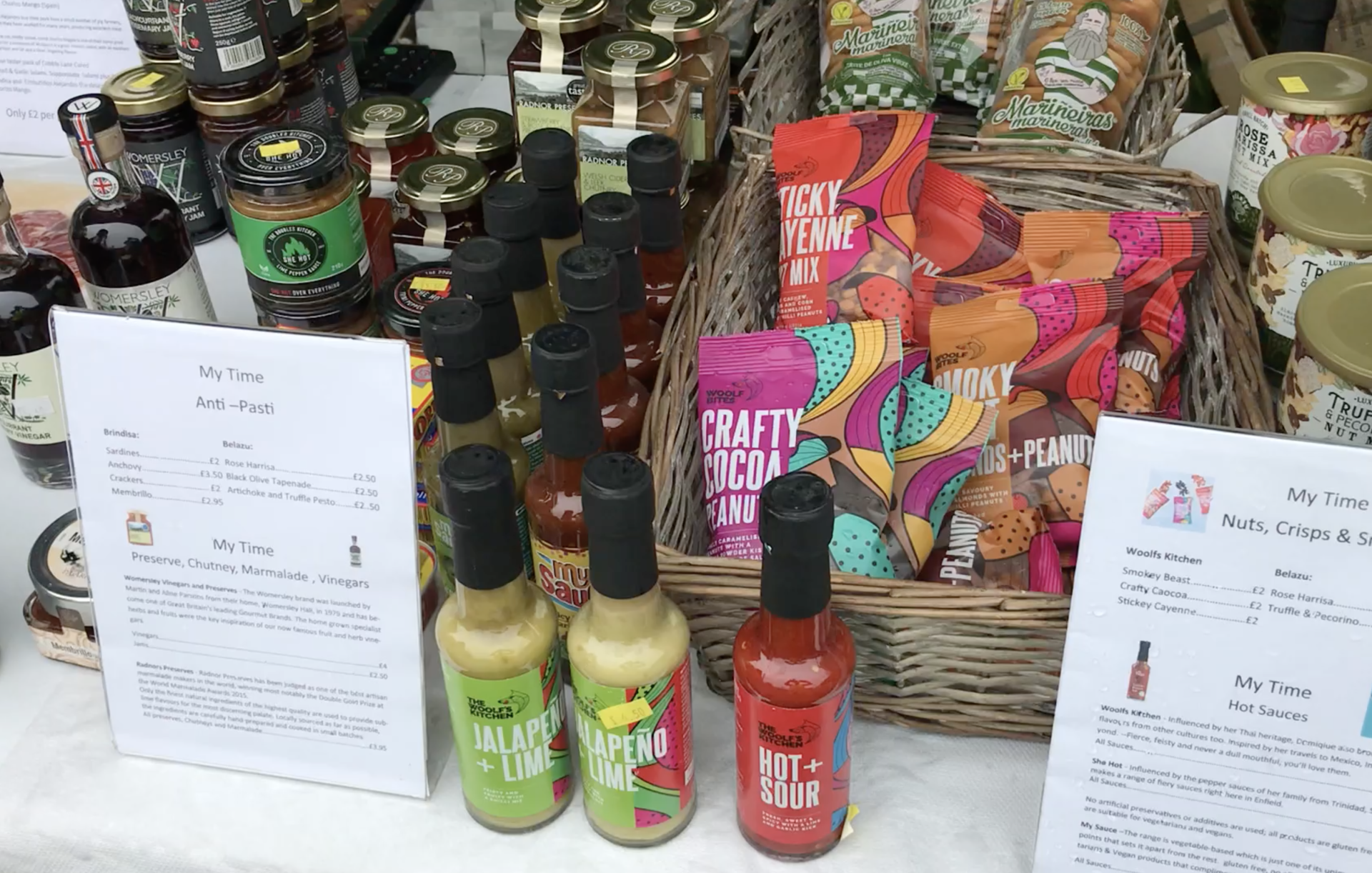 A table topped with bottles of hot sauce and a basket of snacks.