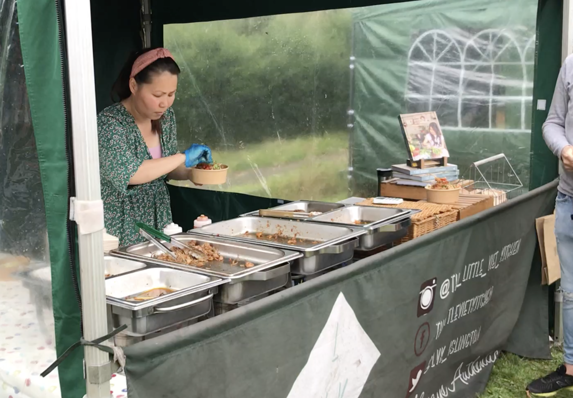 A woman is standing in front of a tent selling food.