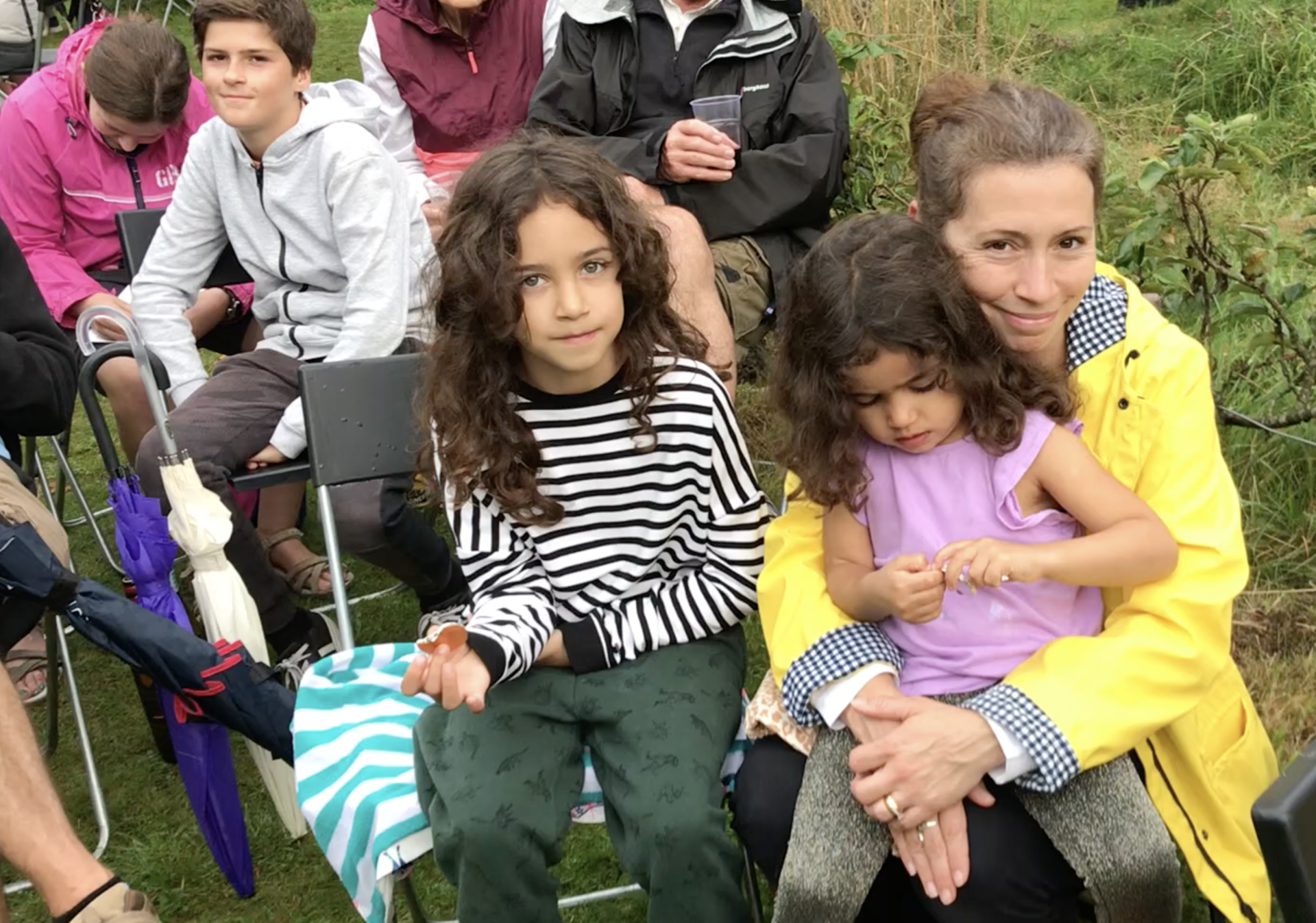 A group of people are sitting in chairs with umbrellas in the grass.