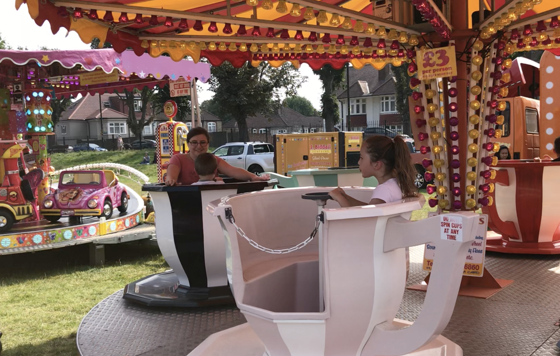 A woman and two children are riding a tea cup ride at a carnival.
