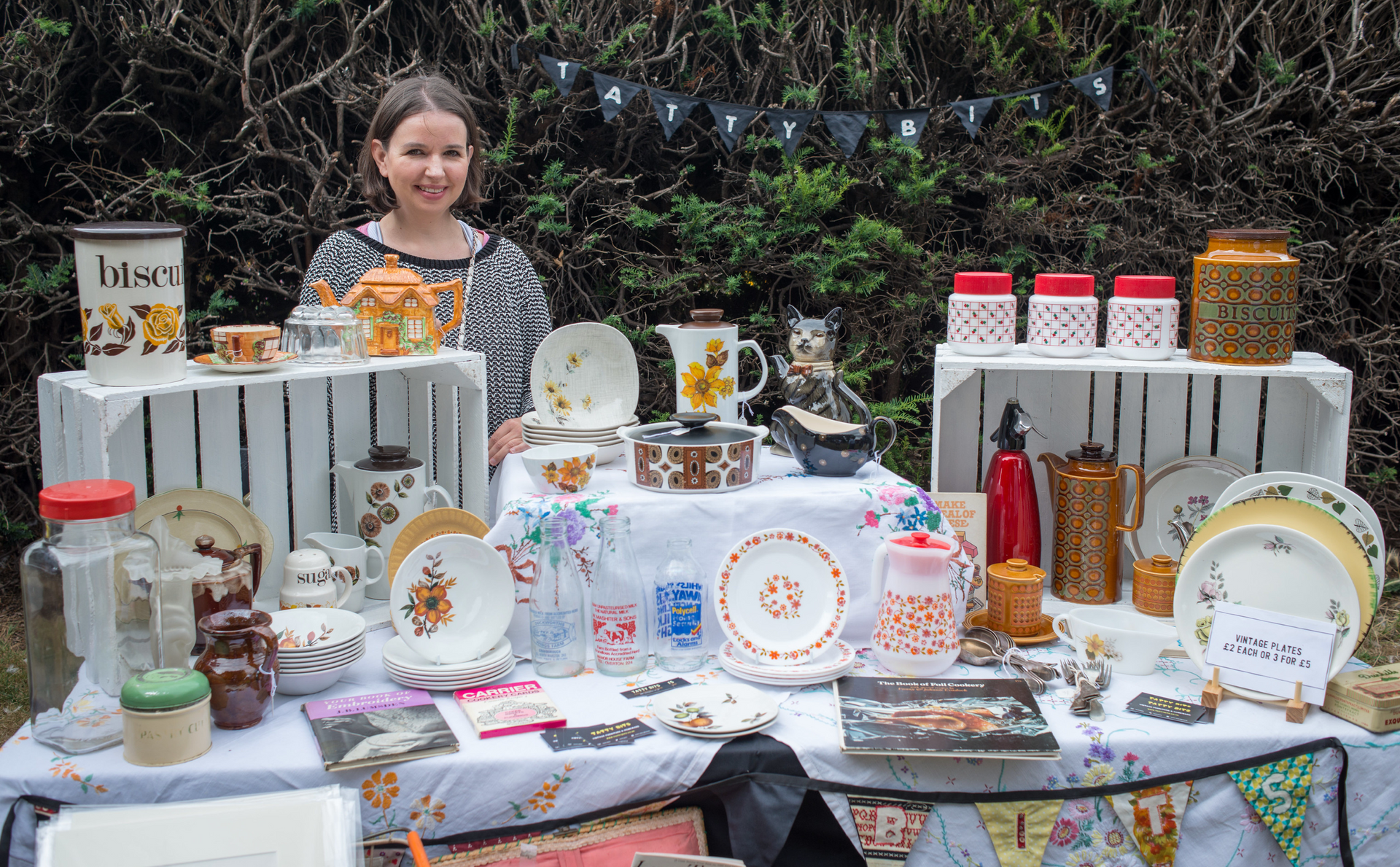 A woman is standing in front of a table filled with plates and jars.